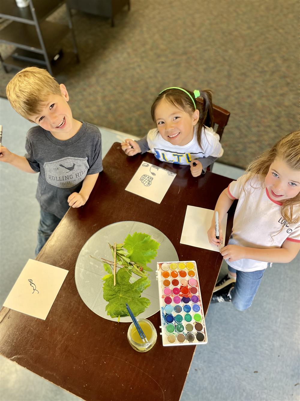 3 students sitting at a table investigating leaves and painting with watercolors 