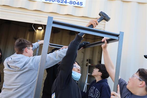 Students building shelving for the storage container to organize materials.