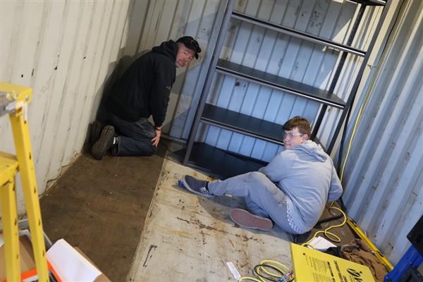 Students building shelving for the storage container to organize materials.