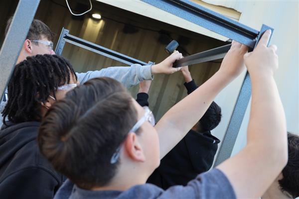 Students building shelving for the storage container to organize materials.