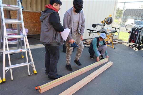 Measuring the wood and using the saw to cut it for the framing.