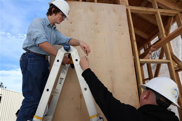 Students installing the moisture barrier to protect the wood of the structure.