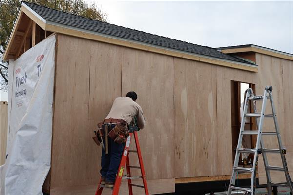 Students installing the moisture barrier to protect the wood of the structure and cutting out windows.