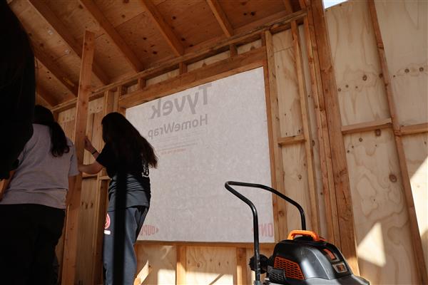 Students installing the moisture barrier to protect the wood of the structure and cutting out windows.
