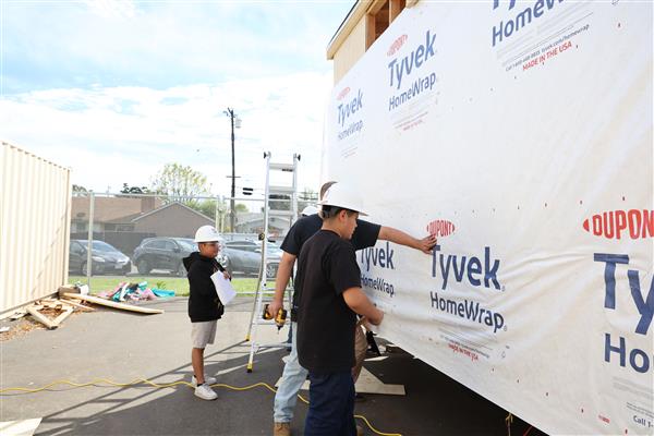 Students installing the moisture barrier to protect the wood of the structure.