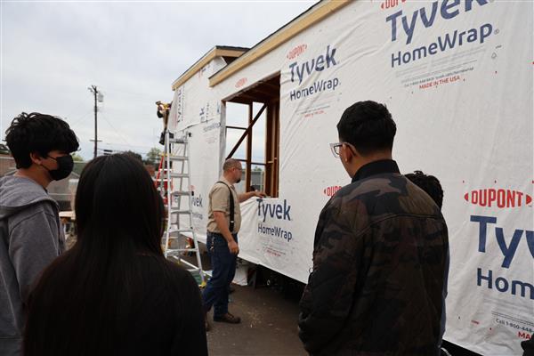 Students installing the moisture barrier to protect the wood of the structure and cutting out windows.