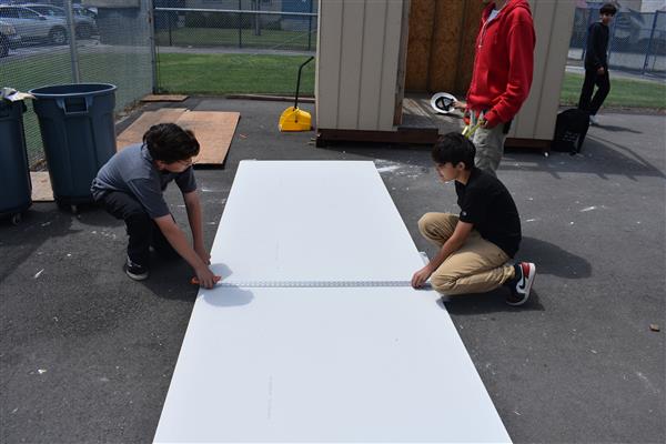 Students measuring and cutting drywall to be installed. 