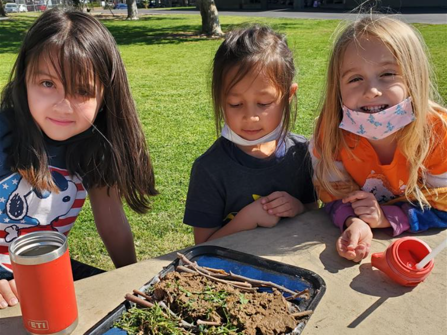 # students smiling with their homemade beaver damn creation on the table in front of them.